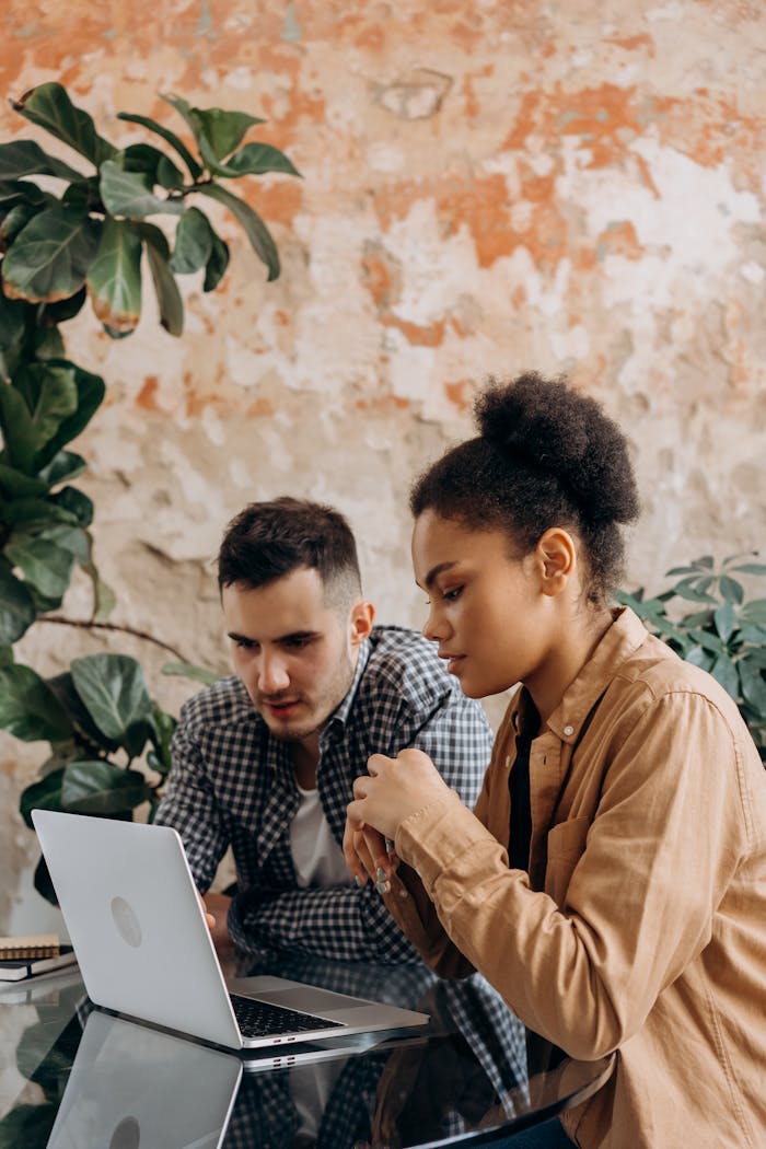 who-we-are Two diverse colleagues discuss work at a laptop indoors, featuring a creative workspace.