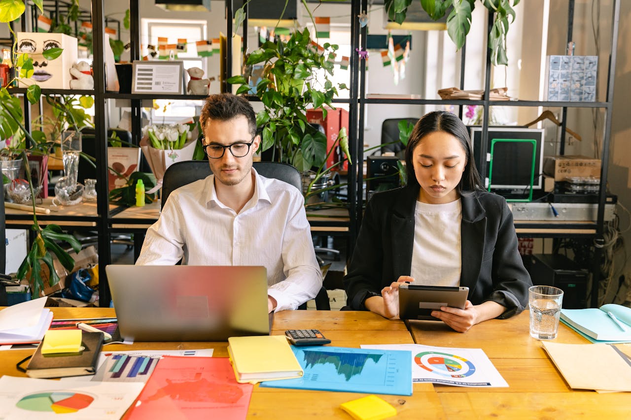 our-story Two professionals working with laptops and tablets in a modern coworking space surrounded by plants.